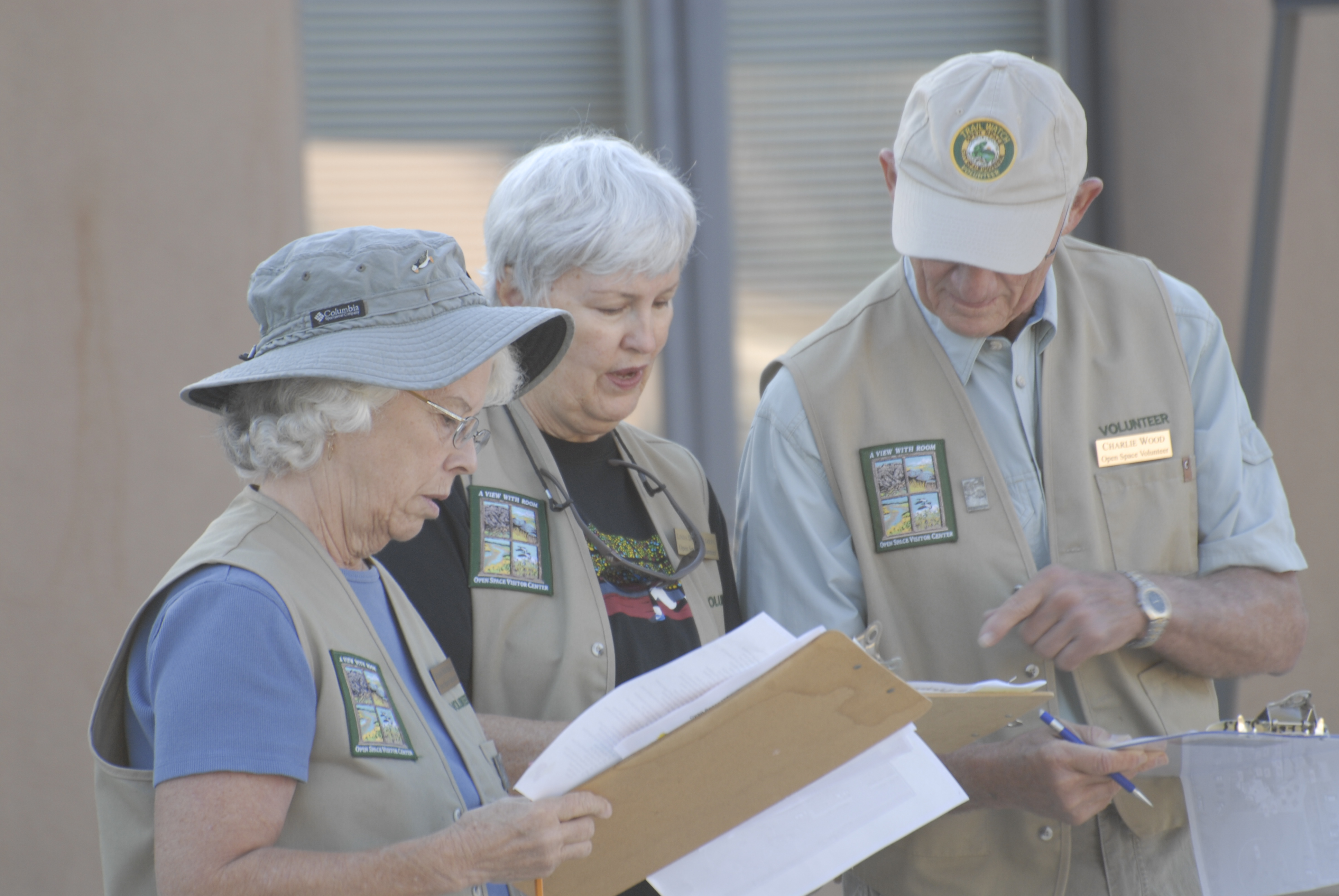 Three Open Space volunteers outside of a building reviewing documents on clipboards.