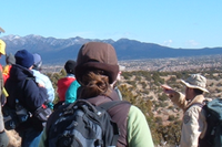 A png of people wearing hats and backpacks looking toward mountains.