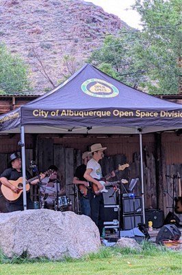 A singer and two guitar players perform under and Open Space canopy.