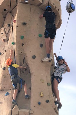 Two youth climb a rock wall wearing helmets and harnesses.