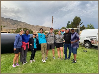A group of City of Albuquerque Parks and Recreation employees standing in a line on the grass at a park and smiling at the camera.