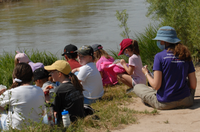 A png of children and an adult sitting next to the Rio Grande river.