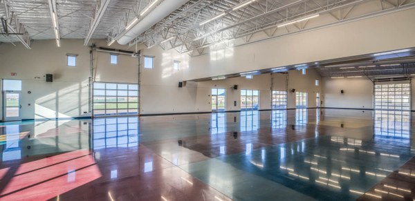 A large open room with shiny floors, rafters on the ceiling and a lot of windows on every wall.