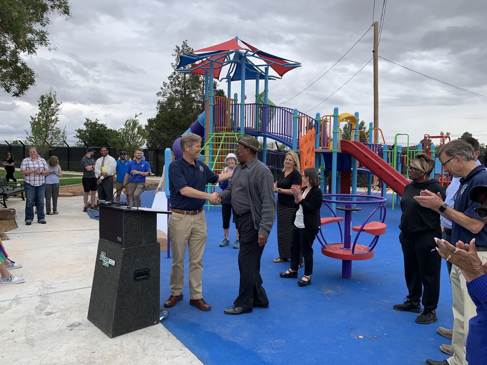 Mayor Keller shaking someone's hand in front of a crowd behind a podium at a park.