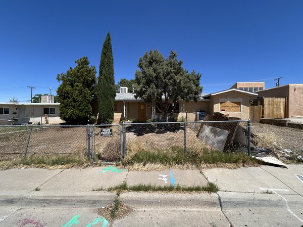 A dilapidated adobe home with boarded up windows.