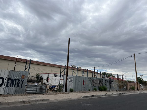 A tan colored two story building behind a damaged metal fence covered in graffiti.