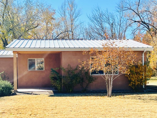 A small house with stucco and a tin roof surrounded by a fall landscape.