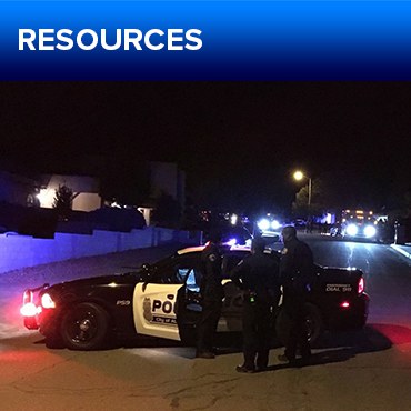 A jpg of the button for the Wellness Resources section, featuring a parked police car with APD officers conversing in front of it, taken at night.