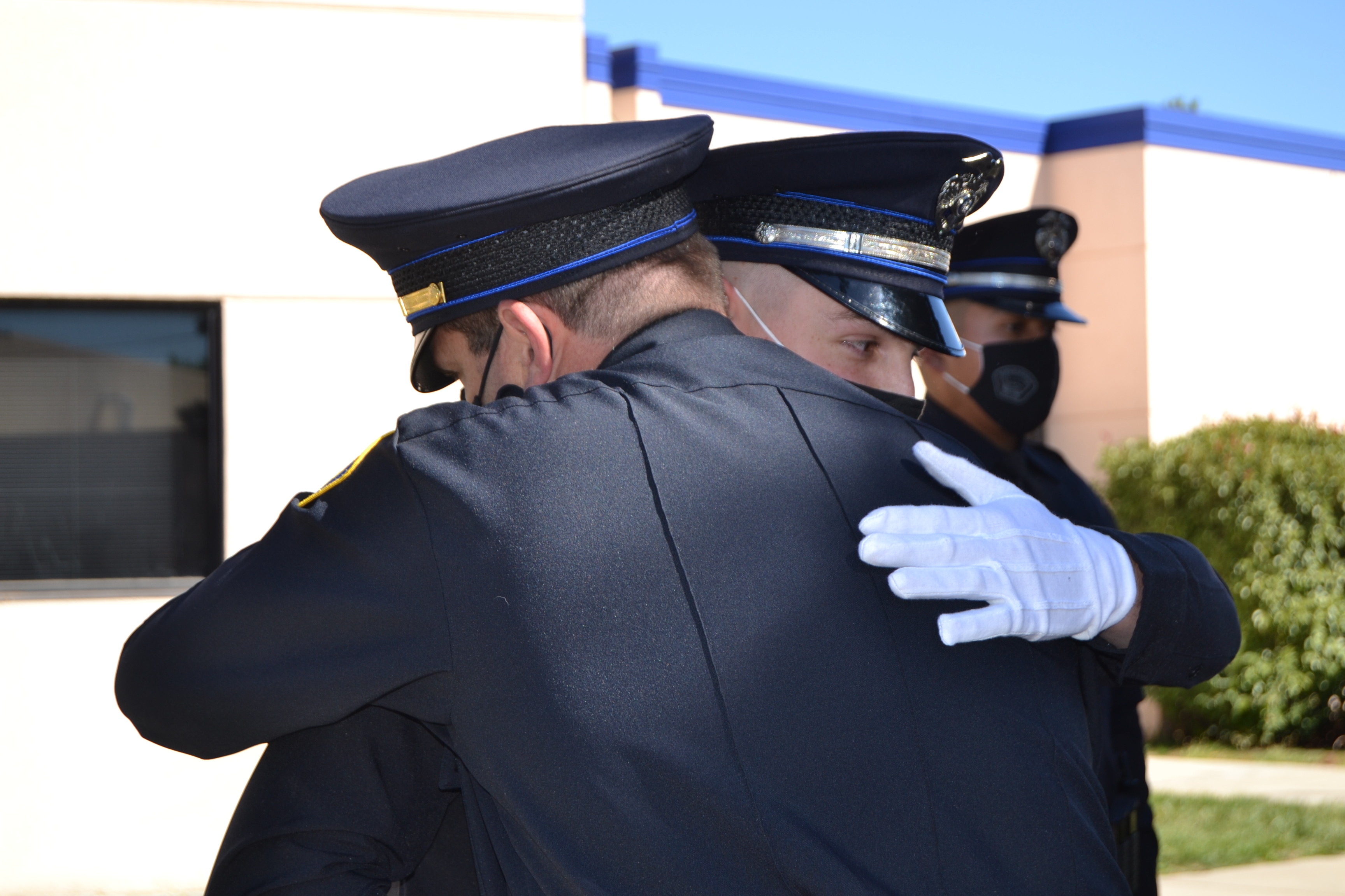 Two officers in formal uniform embracing during an event.