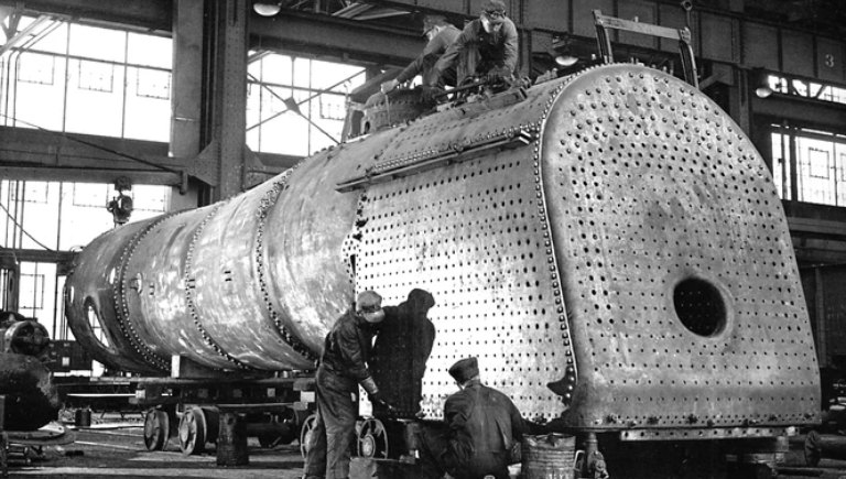 A historic image of rail yard workers conducting maintenance on an engine.