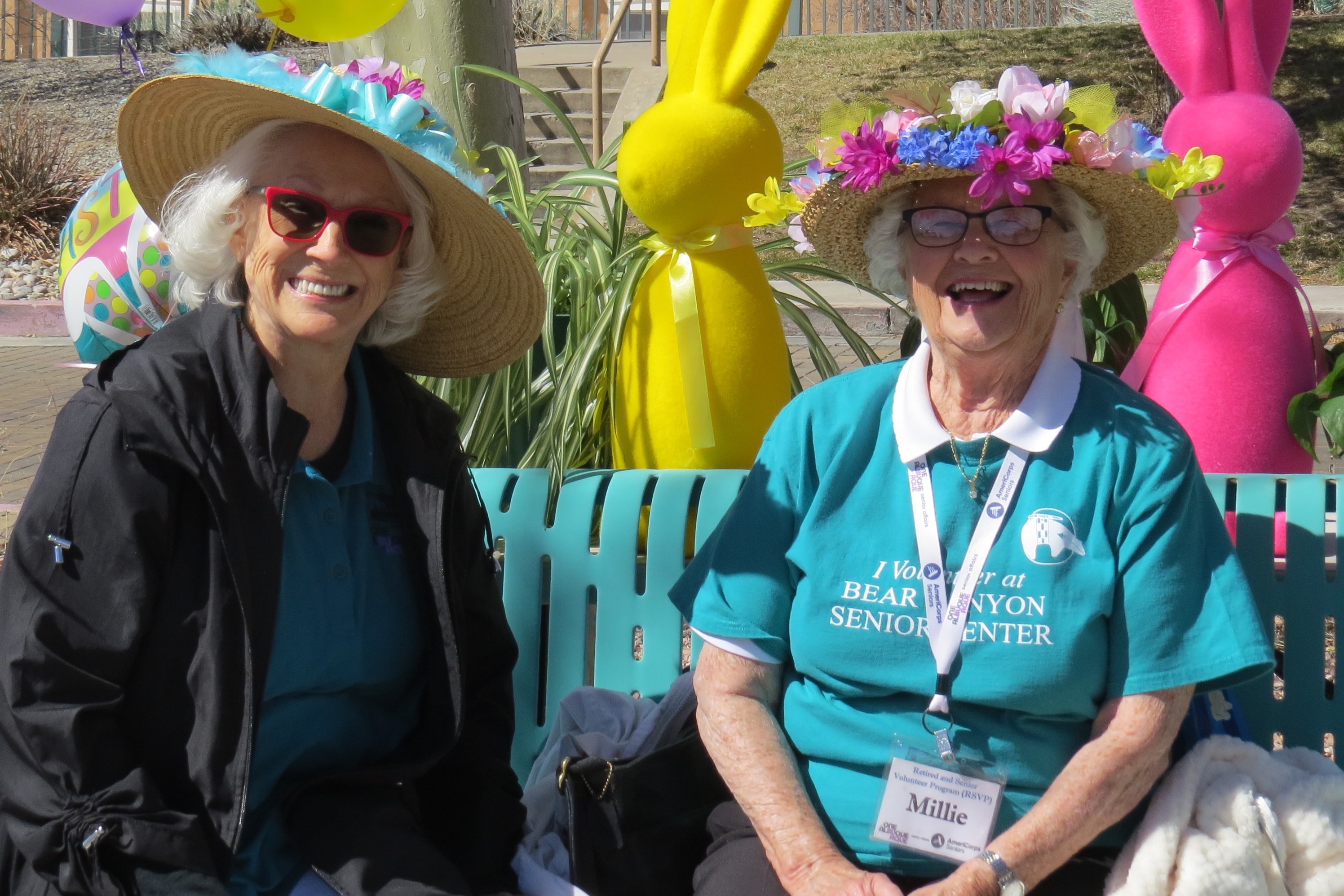 A smiling older woman wearing an AmeriCorps Seniors t-shirt and tie-dye scarf.