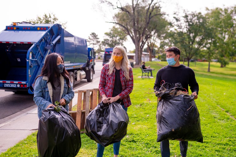 Three young people in masks picking up trash in a park.