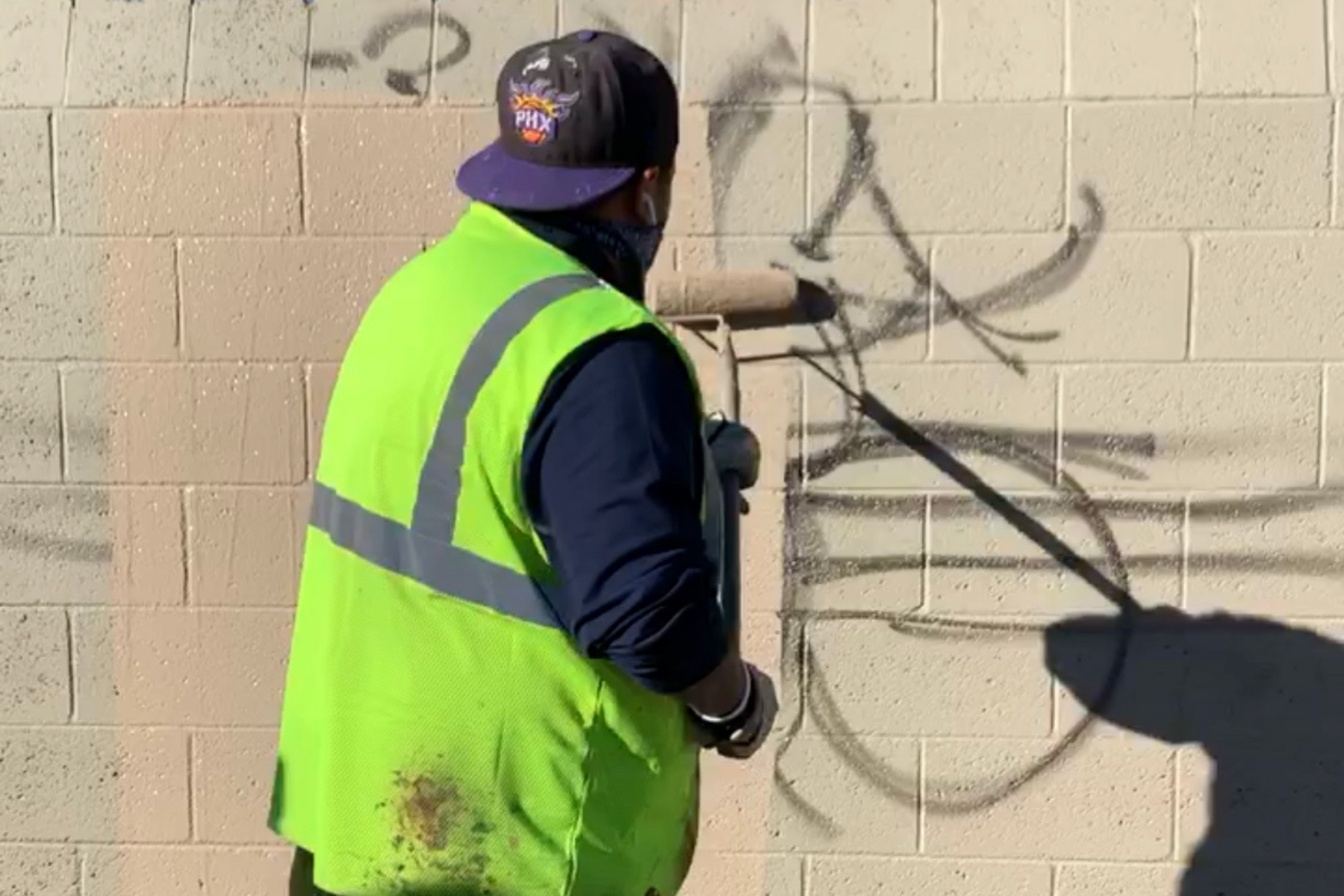 A worker cleaning graffiti from a wall