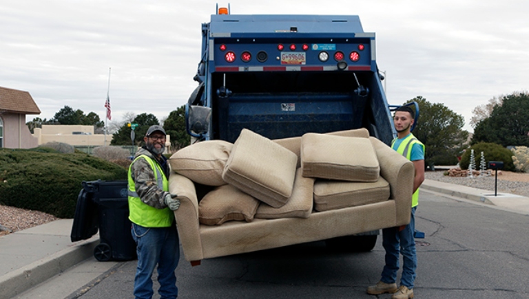 Two SWMD employees placing an old couch into a trash truck.