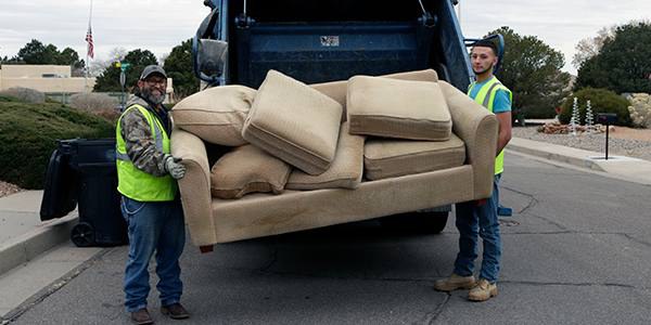 Solid Waste Department employees loading an old couch into a collect truck.