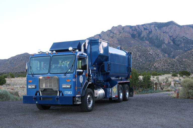 A trash truck in front of the Sandia Mountains