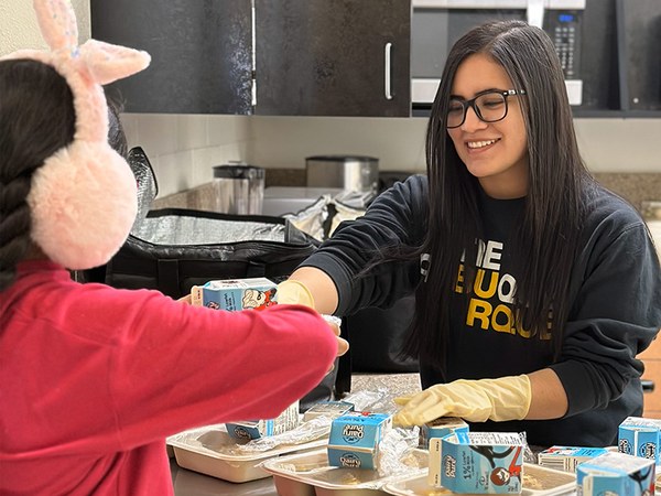 A City of Albuquerque Youth and Family Services staff member hands a child a tray of food.
