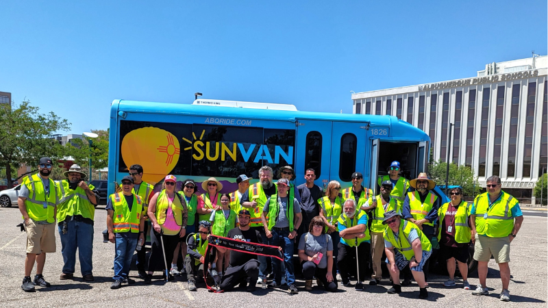 A group of people wearing yellow reflective vests posing in front of an Sun Van with the email address abqride.com on the side.