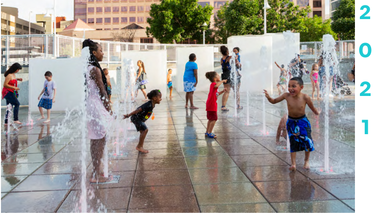 A group of adults observing children playing on the splash pad at Civic Plaza with City Hall in the background.